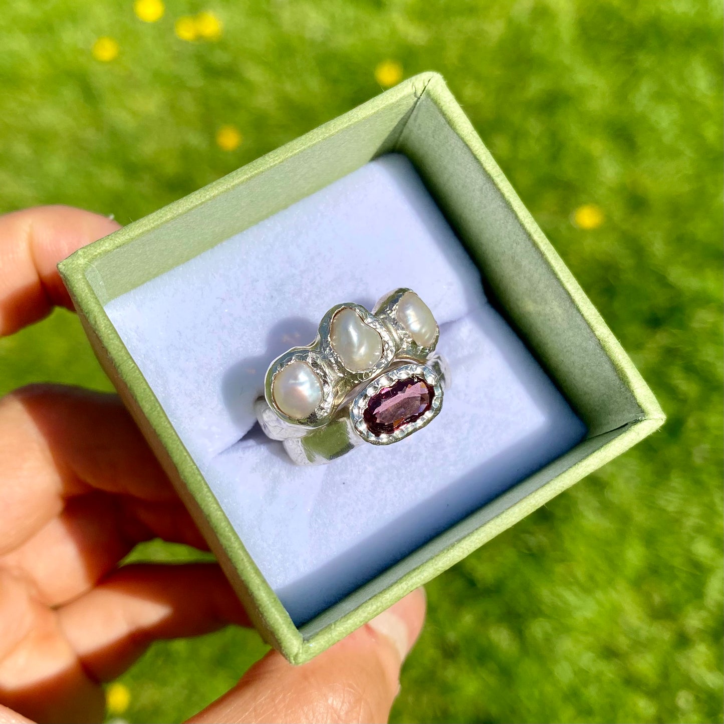 Double Harmony Rings come in a set of two. One ring features a pink tourmaline stone, and the other features three small pearl stones. Handmade from sterling silver, these stacking rings come in a single size: O ½ (or 7 ¼).