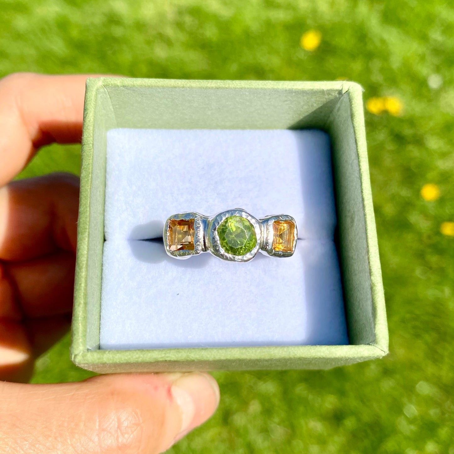 Citrus Garden Ring features a green peridot stone and two square, yellow citrines on the sides. Handmade from sterling silver, this ring comes in a single size: N ½ (or 6 ¾).