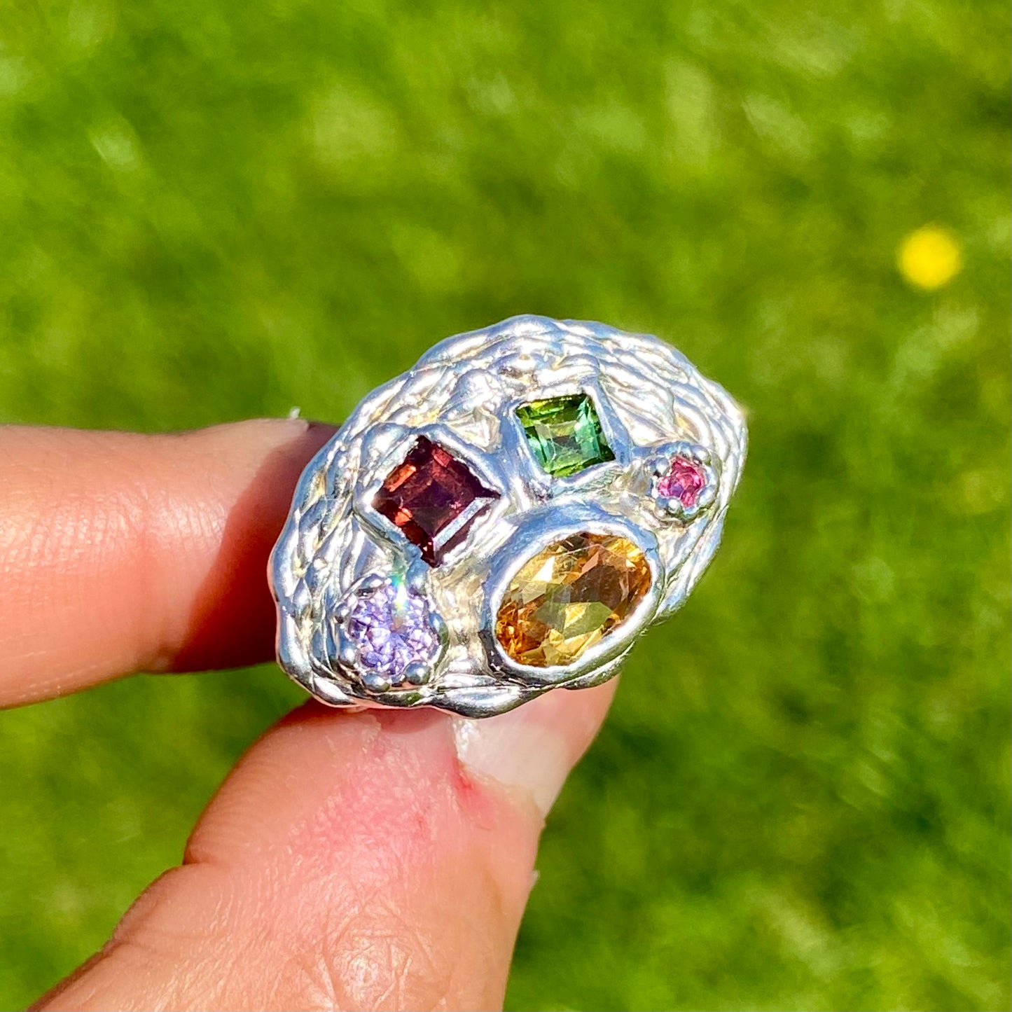 Inspired by a rainbow nestled in a crown, the Crown Rainbow Ring features a dazzling combination of gemstones. An oval yellow citrine gemstone, complemented by pink and green tourmalines, and two light pink and clear stones, all set in a chunky band. Handmade from sterling silver, it comes in a single size: M ½ or 6 ¼.