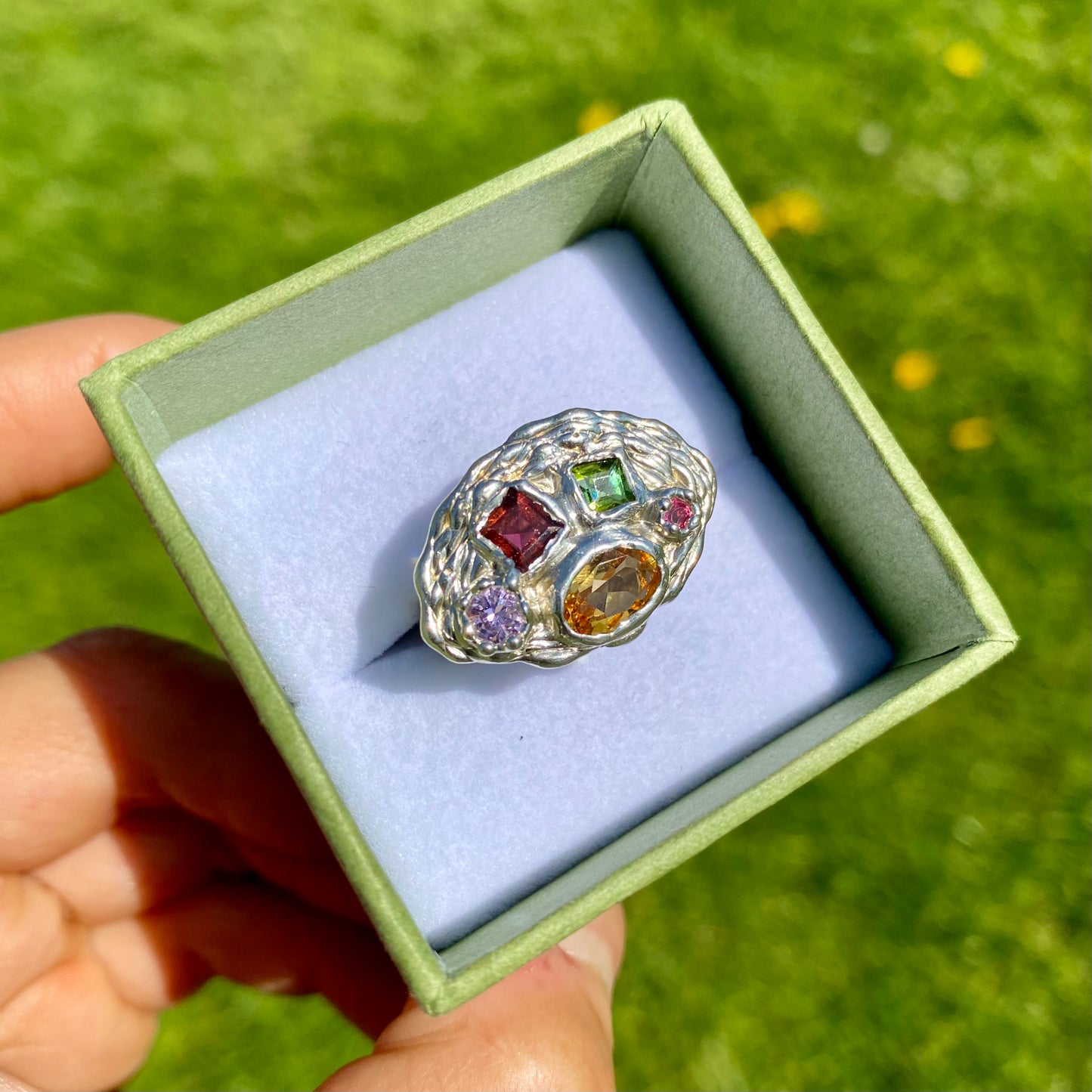 Inspired by a rainbow nestled in a crown, the Crown Rainbow Ring features a dazzling combination of gemstones. An oval yellow citrine gemstone, complemented by pink and green tourmalines, and two light pink and clear stones, all set in a chunky band. Handmade from sterling silver, it comes in a single size: M ½ or 6 ¼.