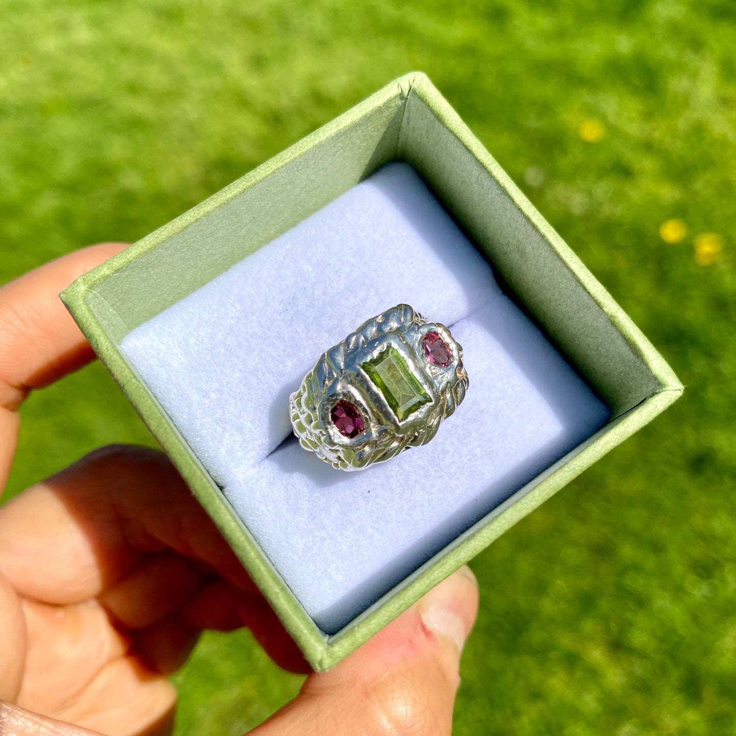 Cute Fish Face Ring features a green peridot stone and two pink tourmalines, set in a chunky band. Handmade from sterling silver, this ring comes in a single size: M ½ (or US size 6 ¼).