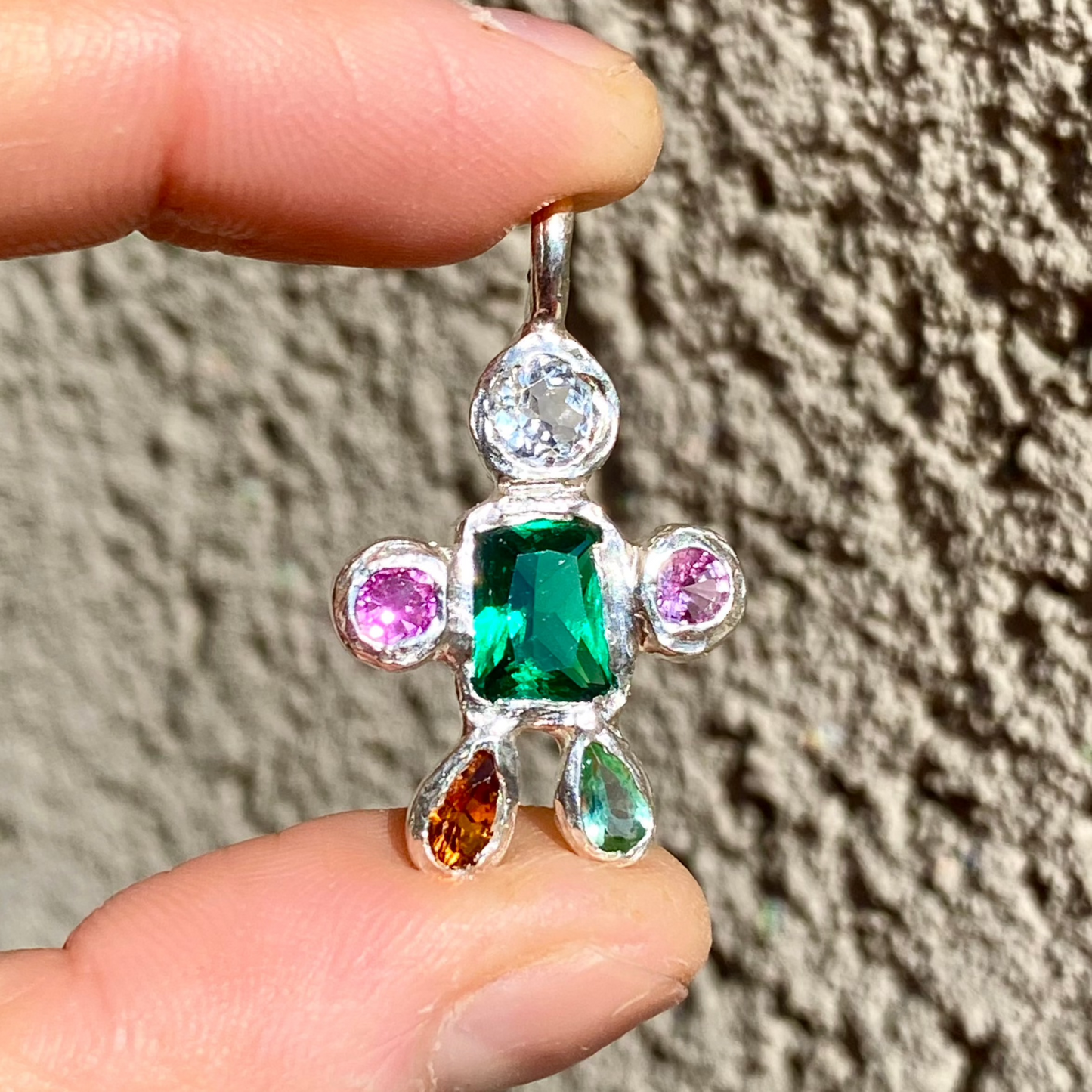 Fairy Light Pendant with green synthetic emerald, CZ, pink sapphires, and tourmalines. Wall as background.