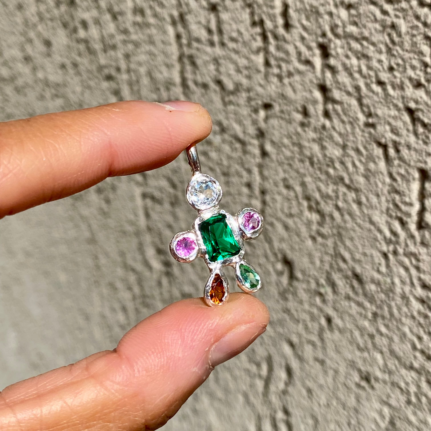Fairy Light Pendant with green synthetic emerald, CZ, pink sapphires, and tourmalines. Wall as background, handmade in Paris