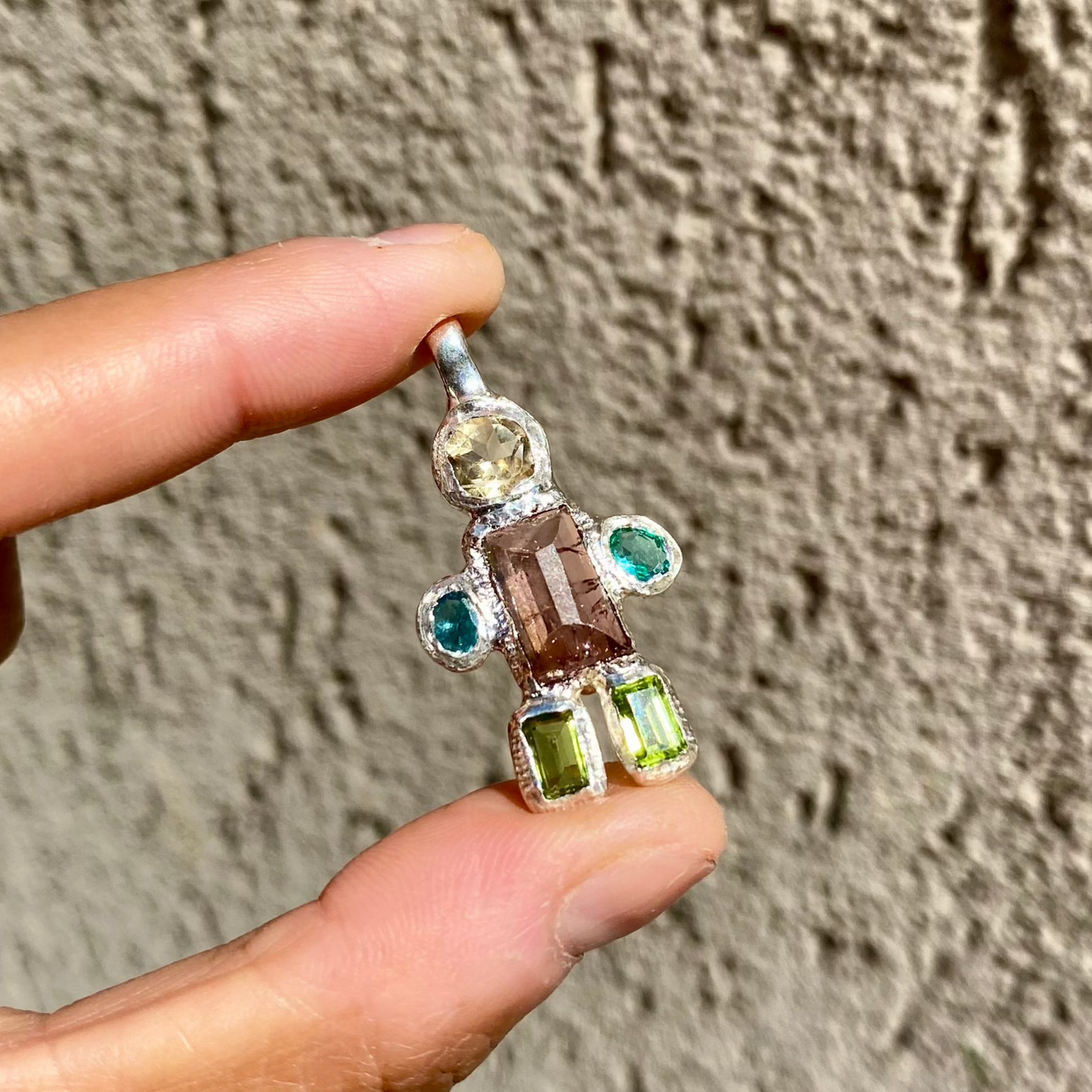 Fairy Light Pendant with green peridots, pink tourmaline, yellow citrine, and green synthetic stones with wall background.