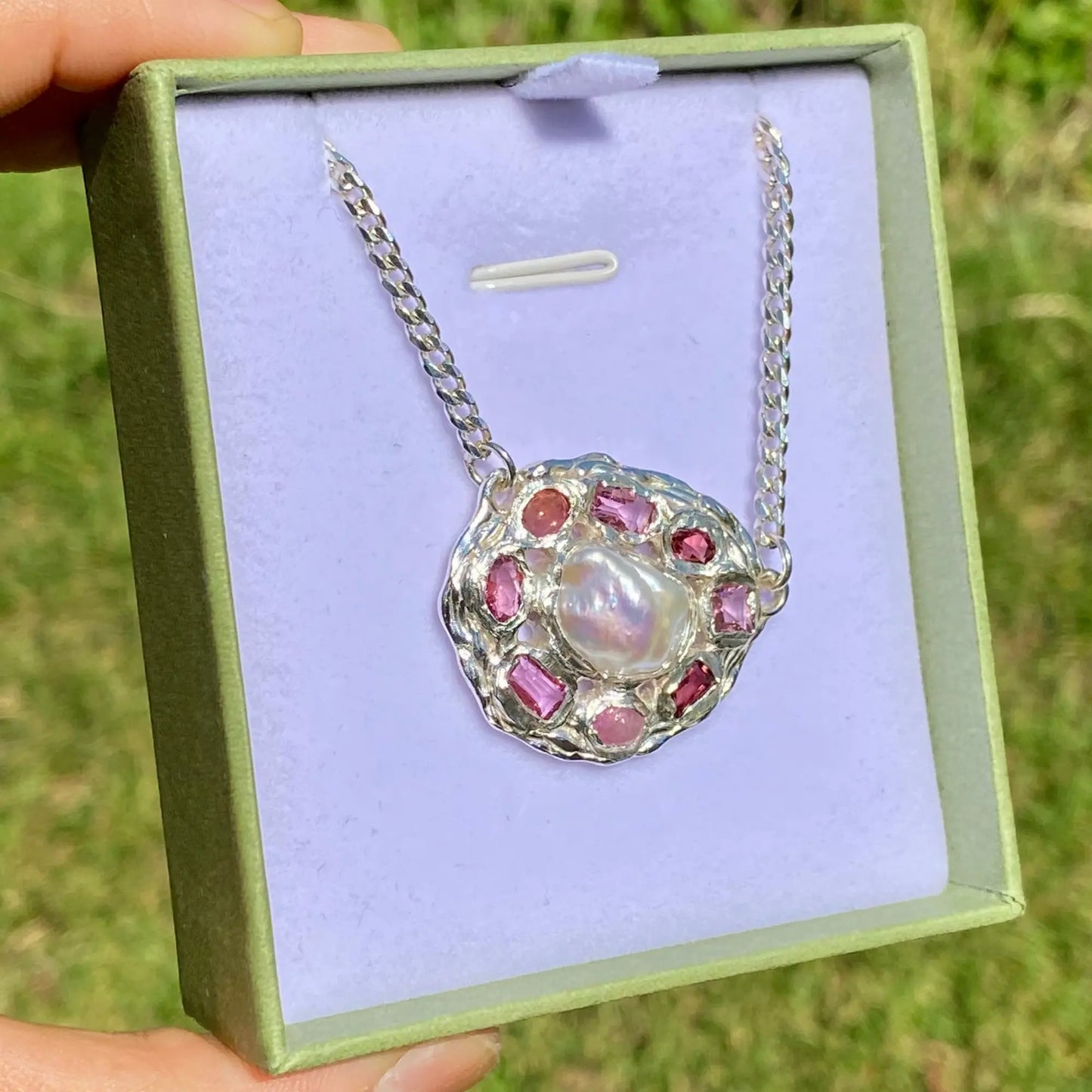 Silver pendant featuring pearls and red stones in a green box.