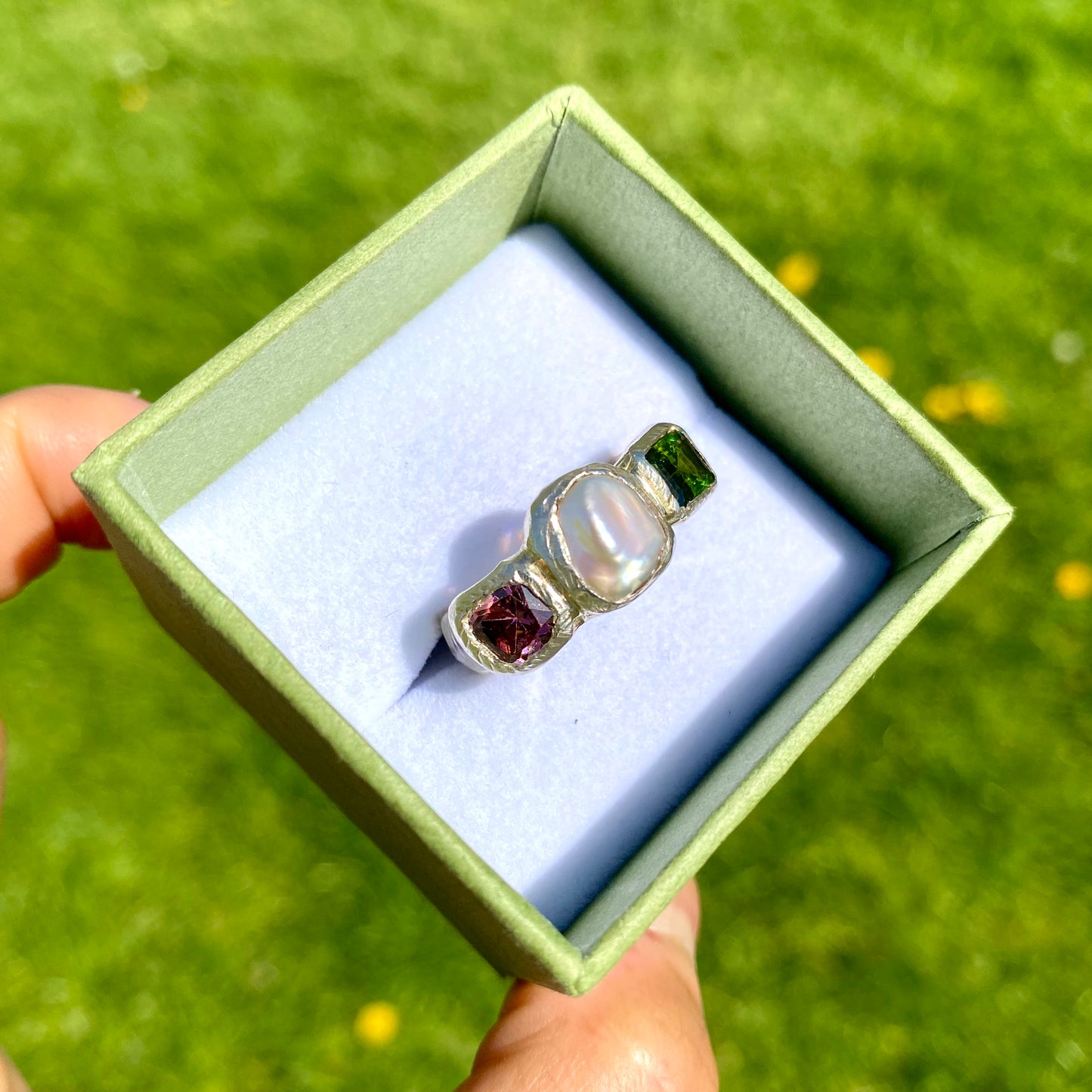 Jewel Tapestry Ring features a pearl, a green tourmaline, and a pink spinel stone. Handmade from sterling silver, this ring comes in a single size: O or 7.