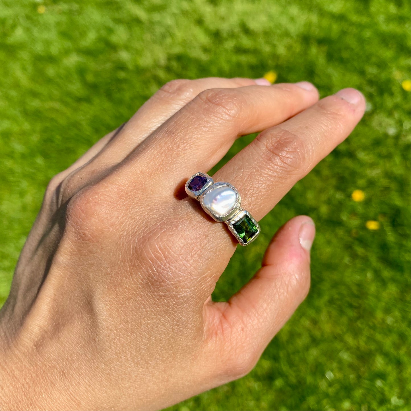 Jewel Tapestry Ring features a pearl, a green tourmaline, and a pink spinel stone. Handmade from sterling silver, this ring comes in a single size: O or 7.