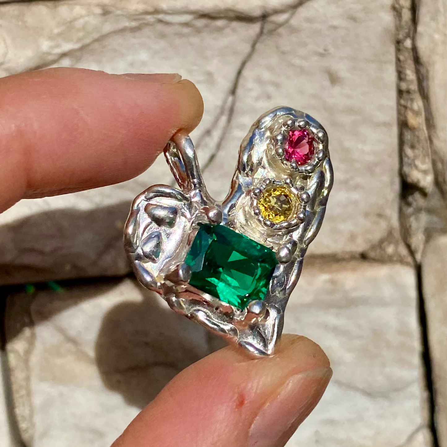 Handmade by Lia from Lia Makes Jewellery, this sterling silver heart-shaped pendant features a unique combination of colourful stones like tourmalines, sapphires, citrine, pink and blue topaz, and tiny synthetic gems, shown in a close-up to highlight the vibrant setting.