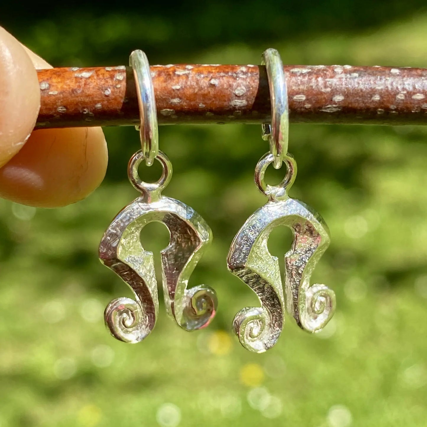 Silver earrings shaped like Mamuli held on a stick with a natural background
