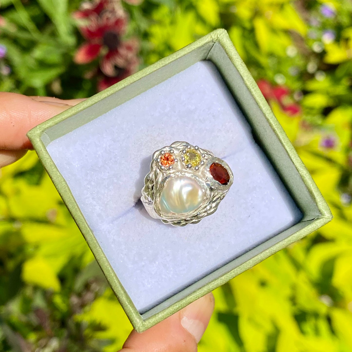 The Melodi features a thick band with four stones: a Keshi pearl, a red garnet, yellow and orange sapphires. The ring is available in size ;O 1/2 (US 7 1/4).