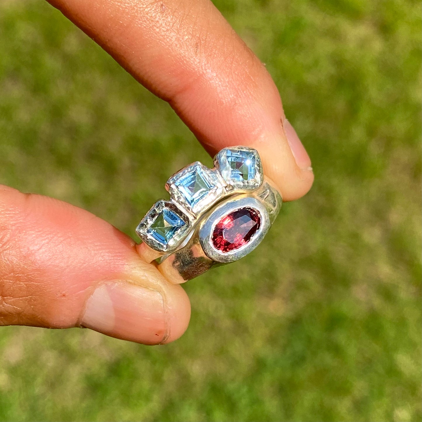The Ocean Blossom ring stack comes as a set of two. One ring features three light blue aquamarine stones, and the other has a red oval garnet stone. Handmade by me from sterling silver, these stacking rings are available in one size: M (US 6)