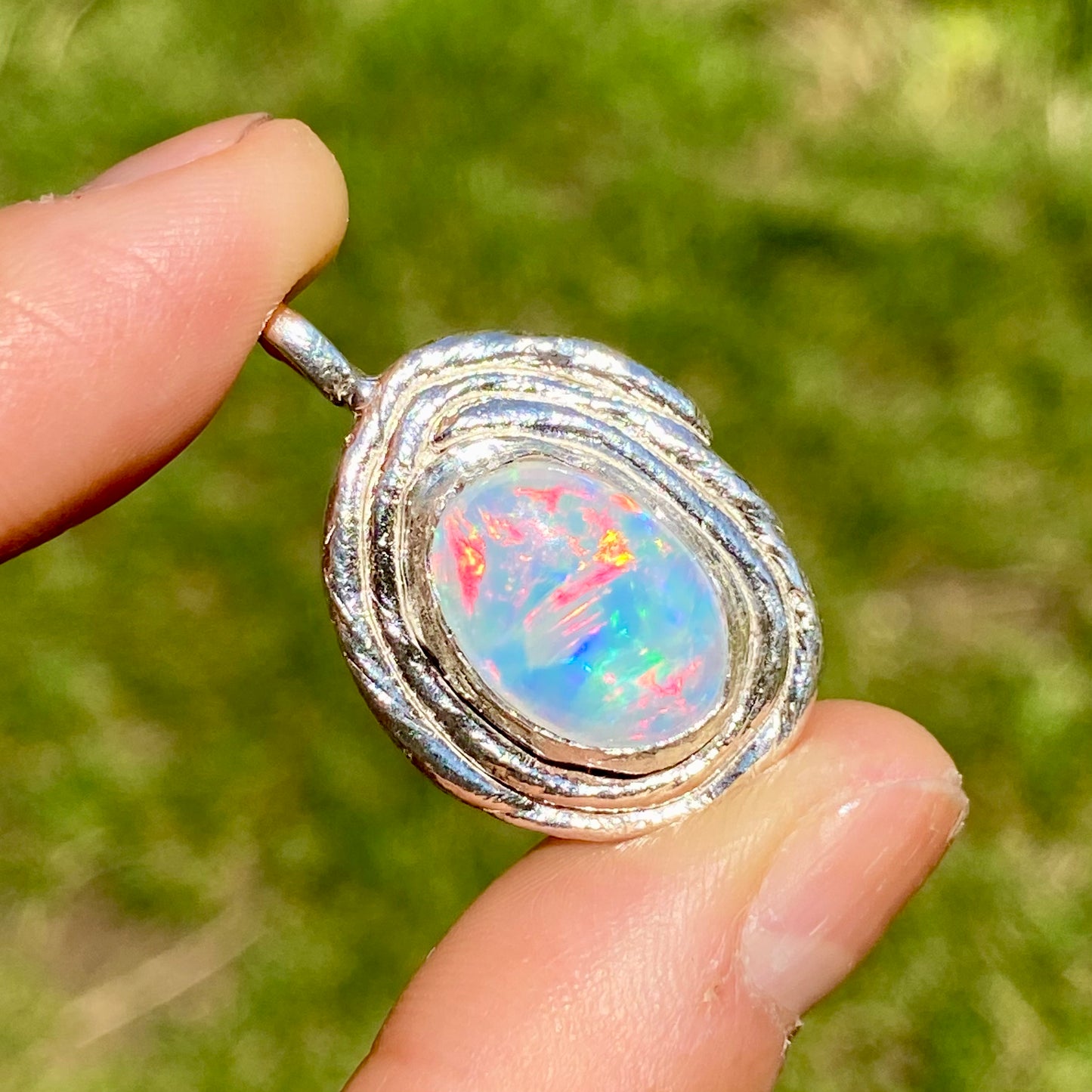 Opal pendant in a silver setting held between fingers with a blurred green background