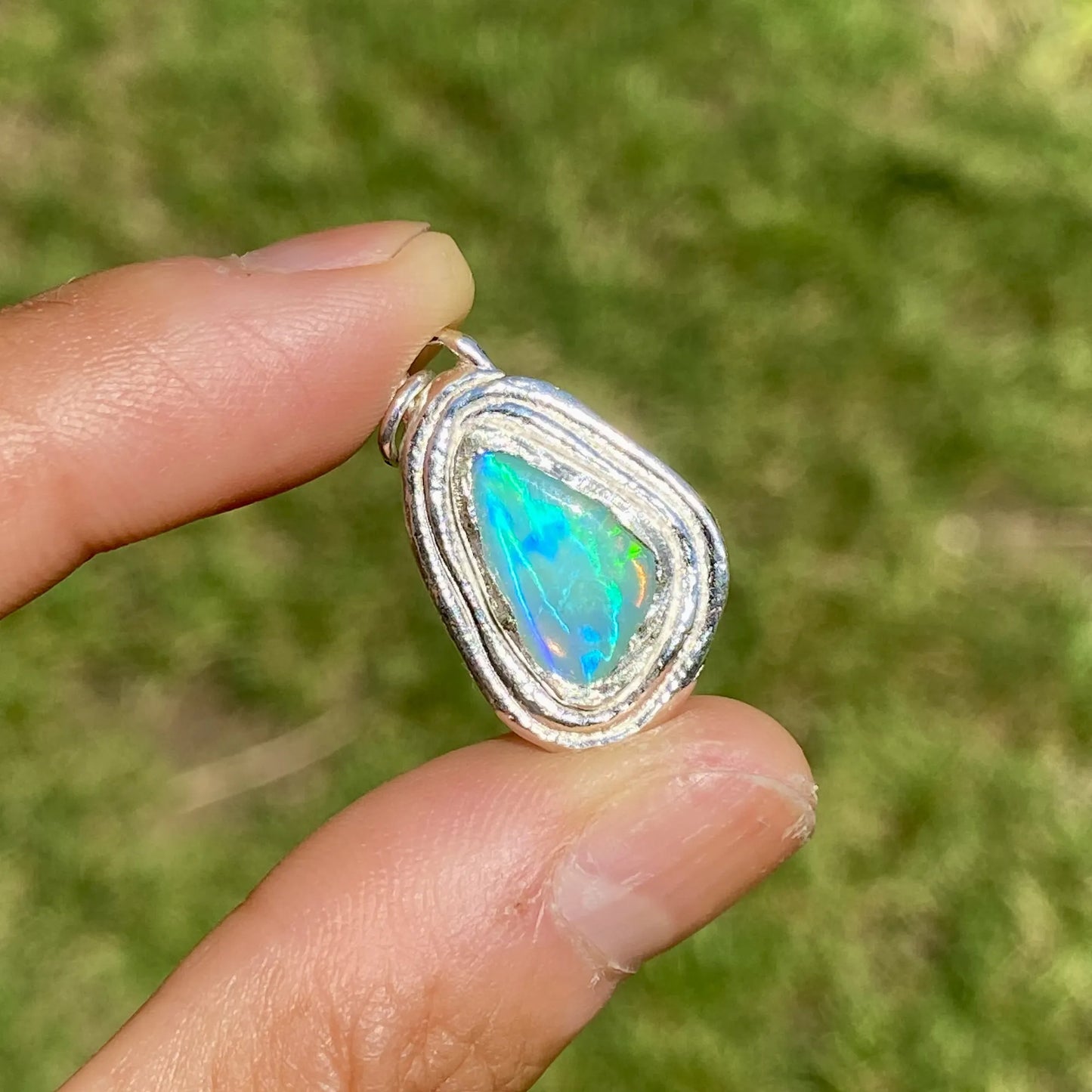 Opal pendant held between fingers with a blurred green background