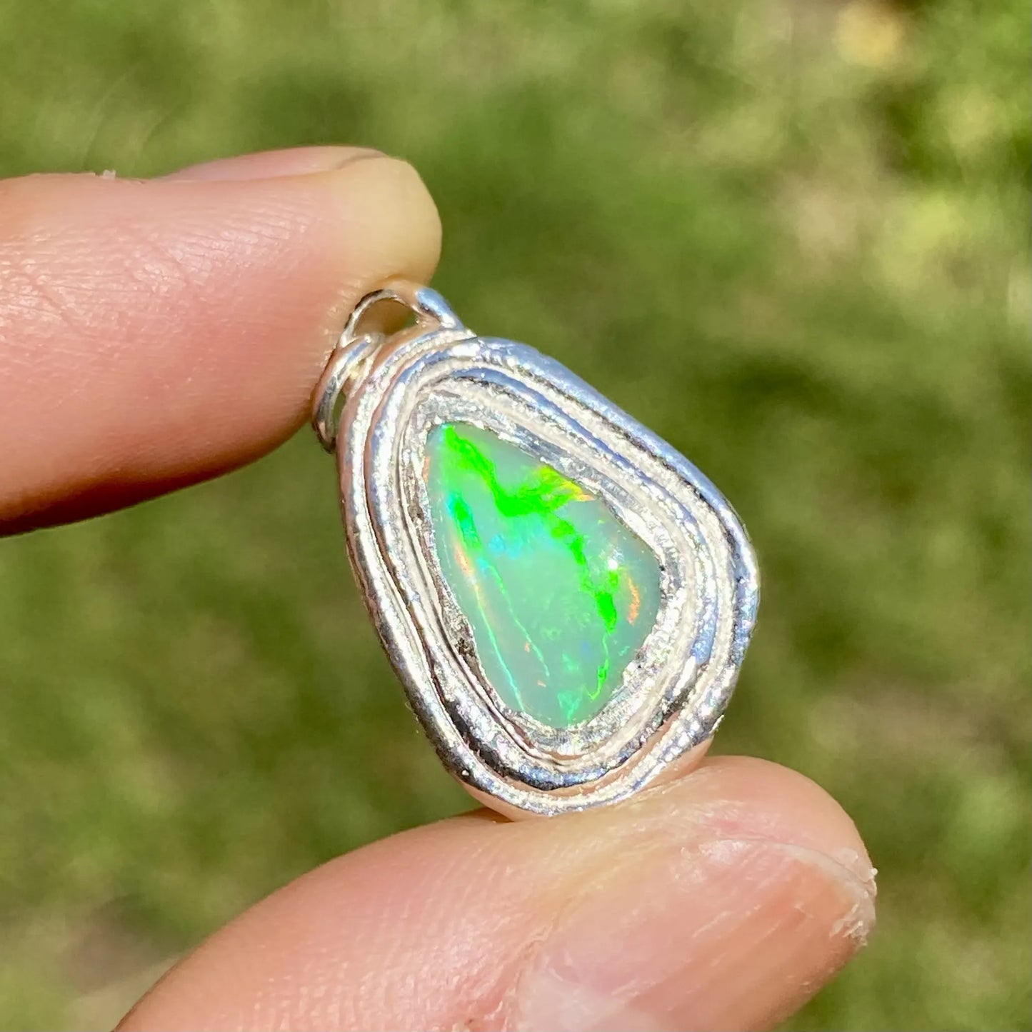 Opal pendant held between fingers with a blurred green background