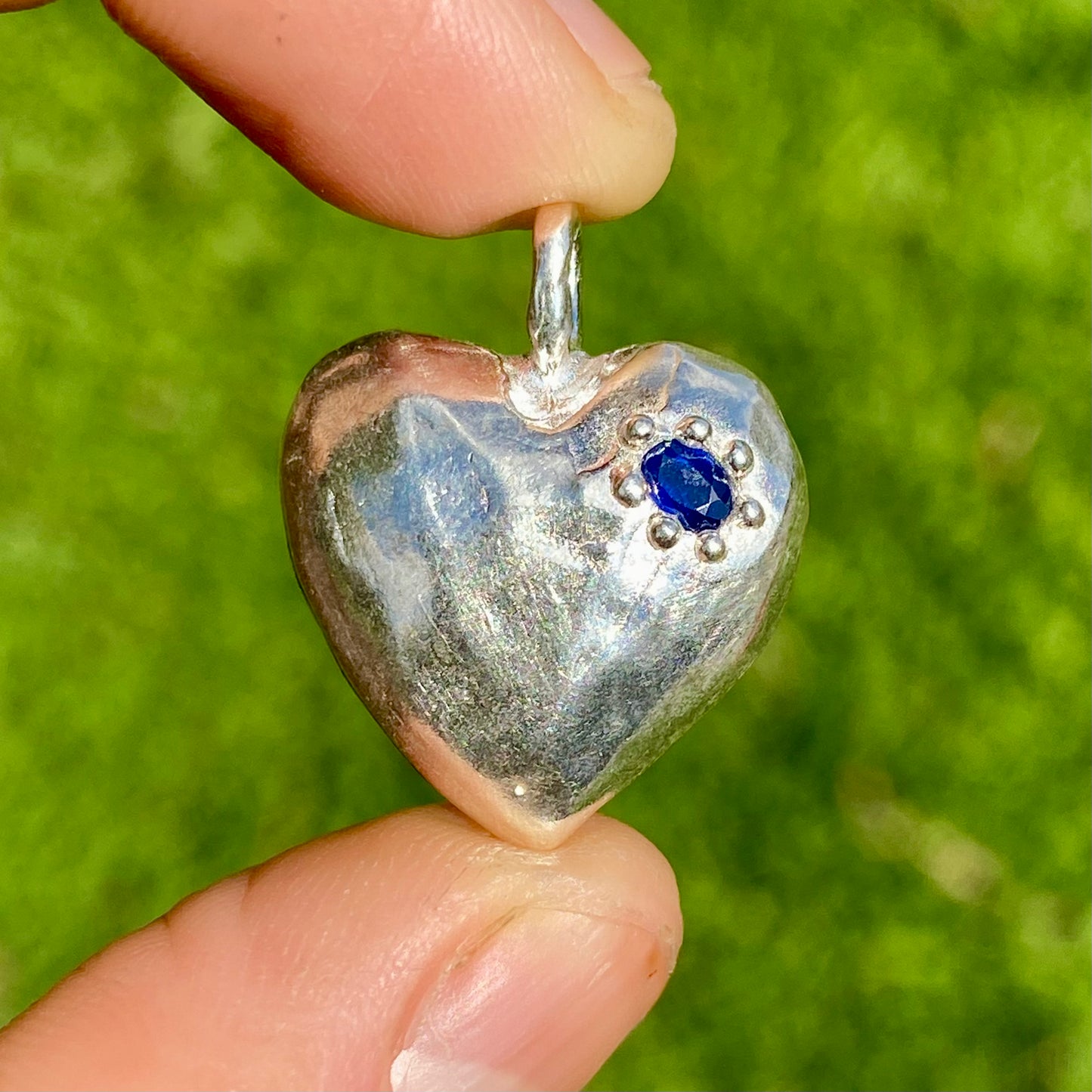 The Petite Heart pendant is a heart-shaped piece, handmade by me in sterling silver. Each pendant features a sapphire stone and is available in four colours: yellow, pink, orange, or blue.