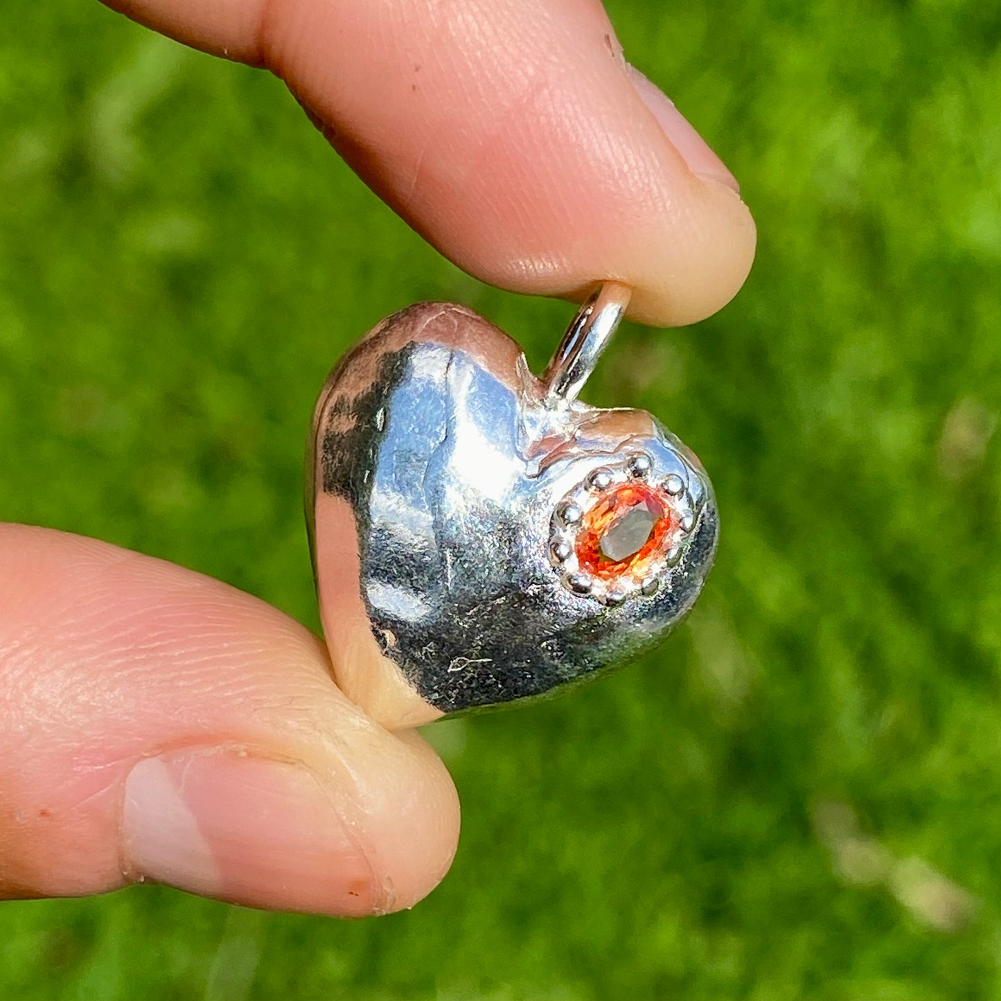 The Petite Heart pendant is a heart-shaped piece, handmade by me in sterling silver. Each pendant features a sapphire stone and is available in four colours: yellow, pink, orange, or blue.