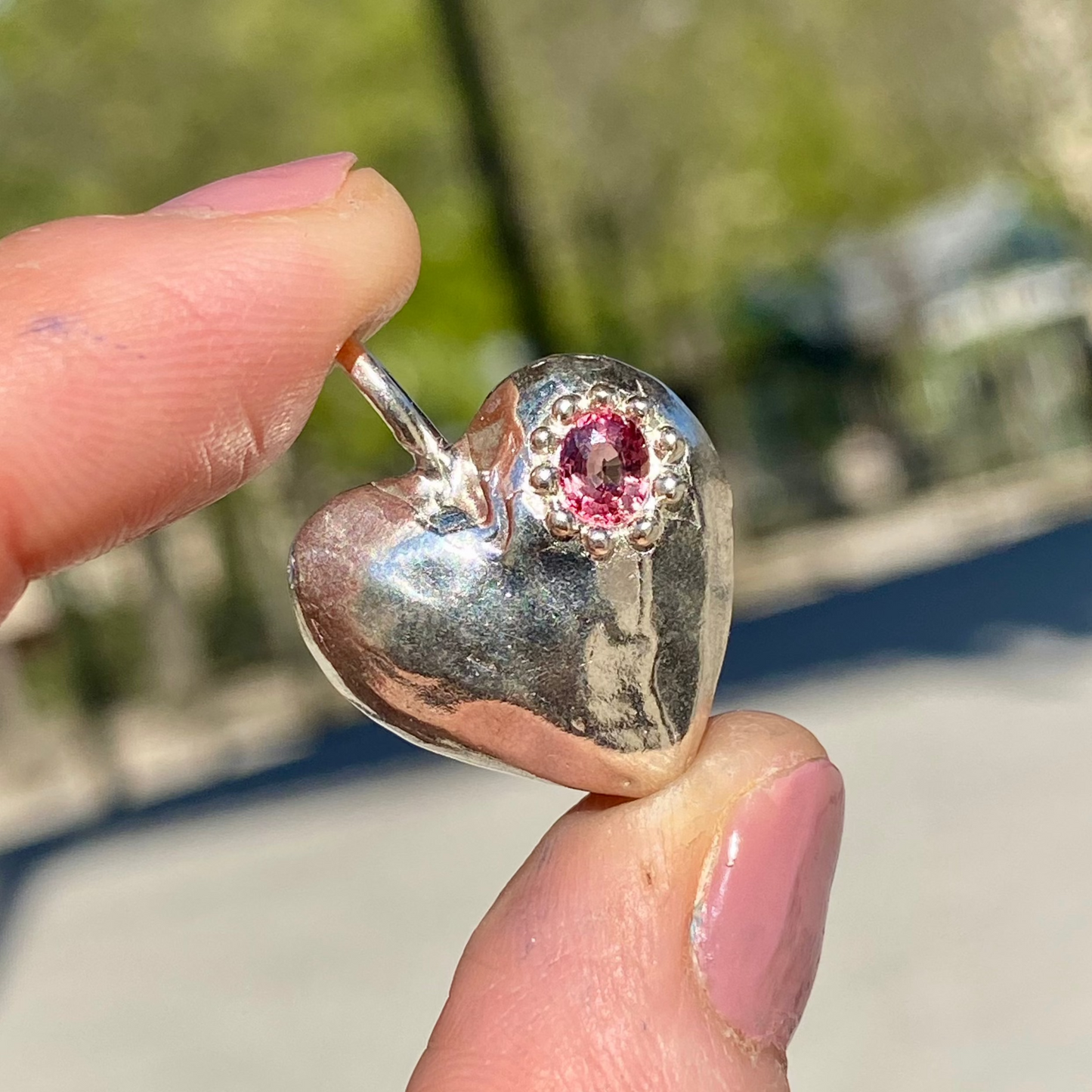 The Petite Heart pendant is a heart-shaped piece, handmade by me in sterling silver. Each pendant features a sapphire stone and is available in four colours: yellow, pink, orange, or blue.