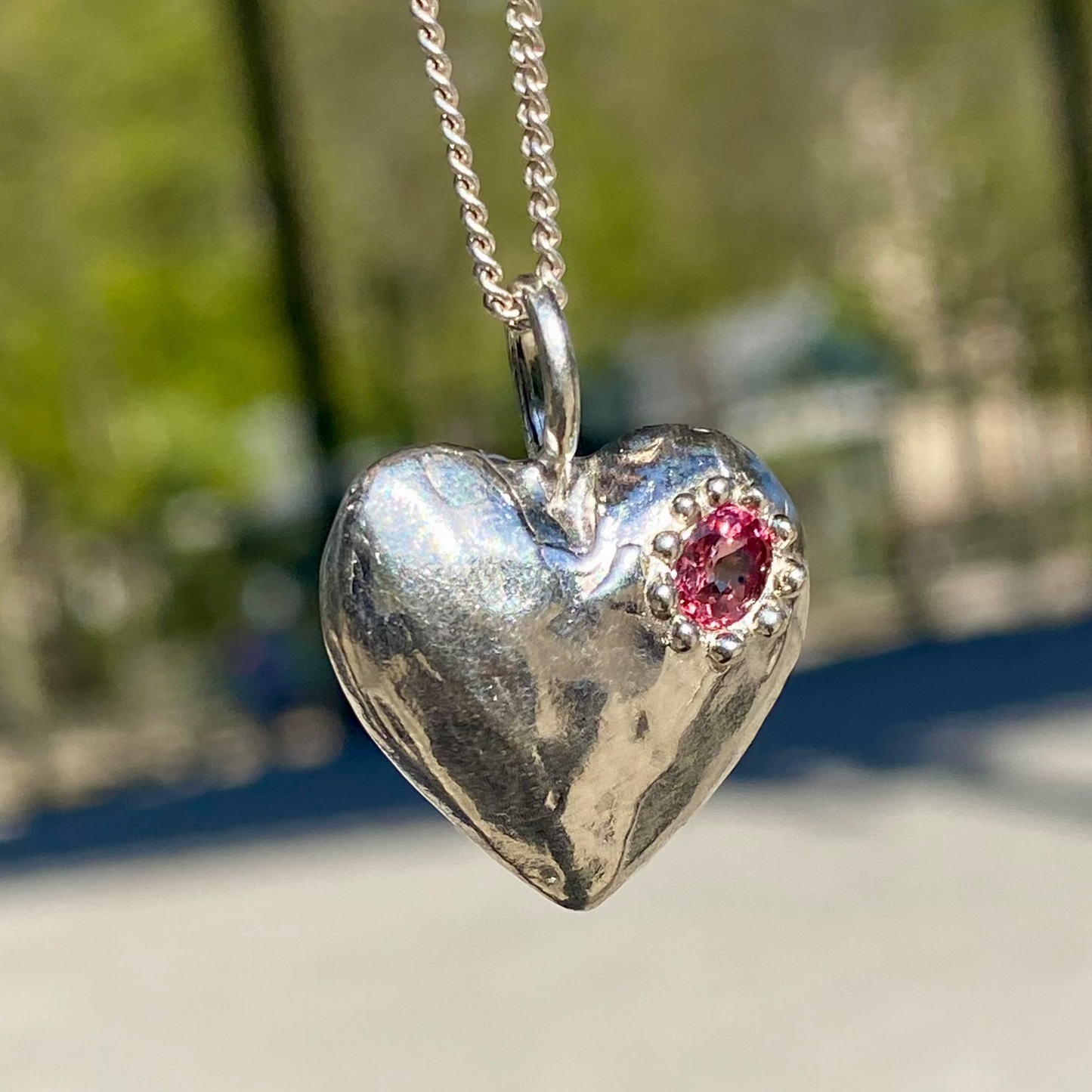 The Petite Heart pendant is a heart-shaped piece, handmade by me in sterling silver. Each pendant features a sapphire stone and is available in four colours: yellow, pink, orange, or blue.