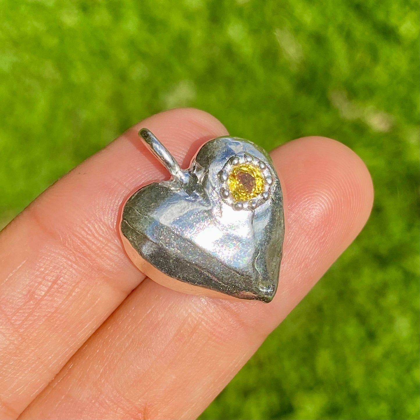 The Petite Heart pendant is a heart-shaped piece, handmade by me in sterling silver. Each pendant features a sapphire stone and is available in four colours: yellow, pink, orange, or blue.