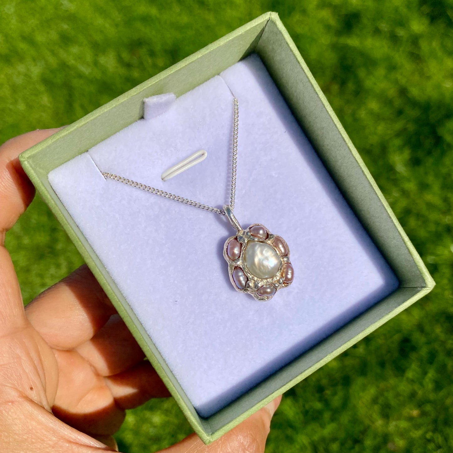 Sakura Bloom Pendant is a handcrafted pendant featuring a white keshi pearl at its center, surrounded by a cluster of six delicate pink pearls. This design evokes the delicate beauty of springtime cherry blossoms in full bloom.