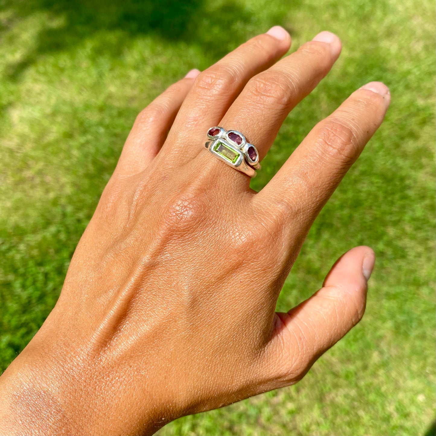 The Spring Blossom ring stack comes as a set of two. One ring features three pink tourmaline stones, and the other has a long green rectangular peridot stone. Handmade from sterling silver, these stacking rings are available in one size: O ½ (US 7 ¼).
