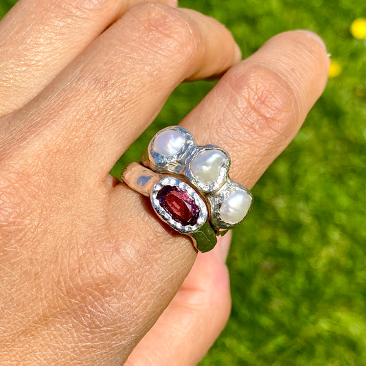Double Harmony Rings come in a set of two. One ring features a pink tourmaline stone, and the other features three small pearl stones. Handmade from sterling silver, these stacking rings come in a single size: O ½ (or 7 ¼).