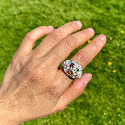 Inspired by a rainbow nestled in a crown, the Crown Rainbow Ring features a dazzling combination of gemstones. An oval yellow citrine gemstone, complemented by pink and green tourmalines, and two light pink and clear stones, all set in a chunky band. Handmade from sterling silver, it comes in a single size: M ½  or 6 ¼. 