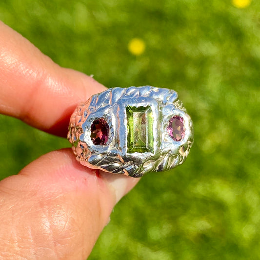 Cute Fish Face Ring features a green peridot stone and two pink tourmalines, set in a chunky band. Handmade from sterling silver, this ring comes in a single size: M ½ (or US size 6 ¼).