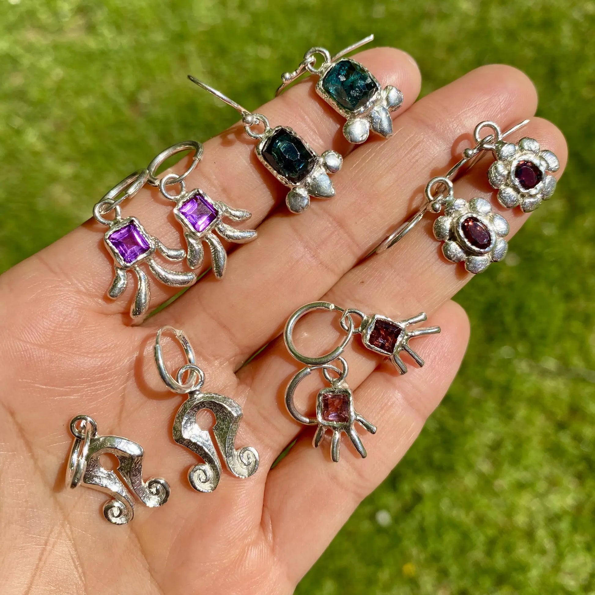 Silver earrings with gemstones held in a hand against a green background