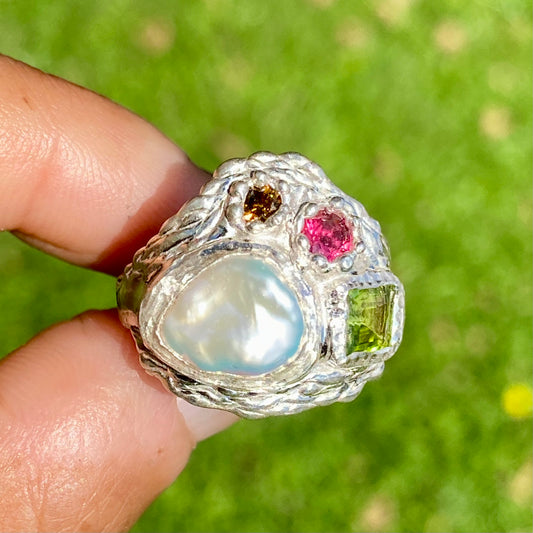 The Harmony features a thick band with four stones: a keshi pearl, a green peridot, pink and orange. Handmade by me, this ring is available in size N (US 6 1/2).&nbsp;
