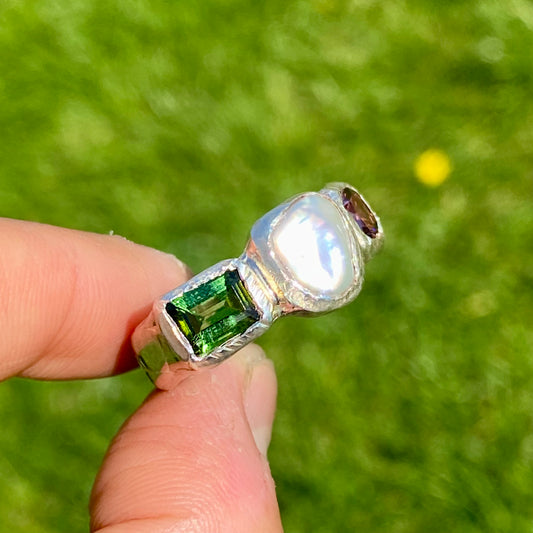 Jewel Tapestry Ring features a pearl, a green tourmaline, and a pink spinel stone. Handmade from sterling silver, this ring comes in a single size: O or 7.
