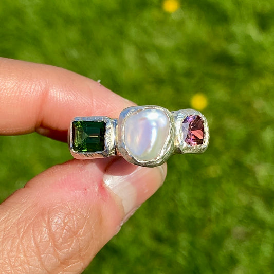 Jewel Tapestry Ring features a pearl, a green tourmaline, and a pink spinel stone. Handmade from sterling silver, this ring comes in a single size: O or 7.