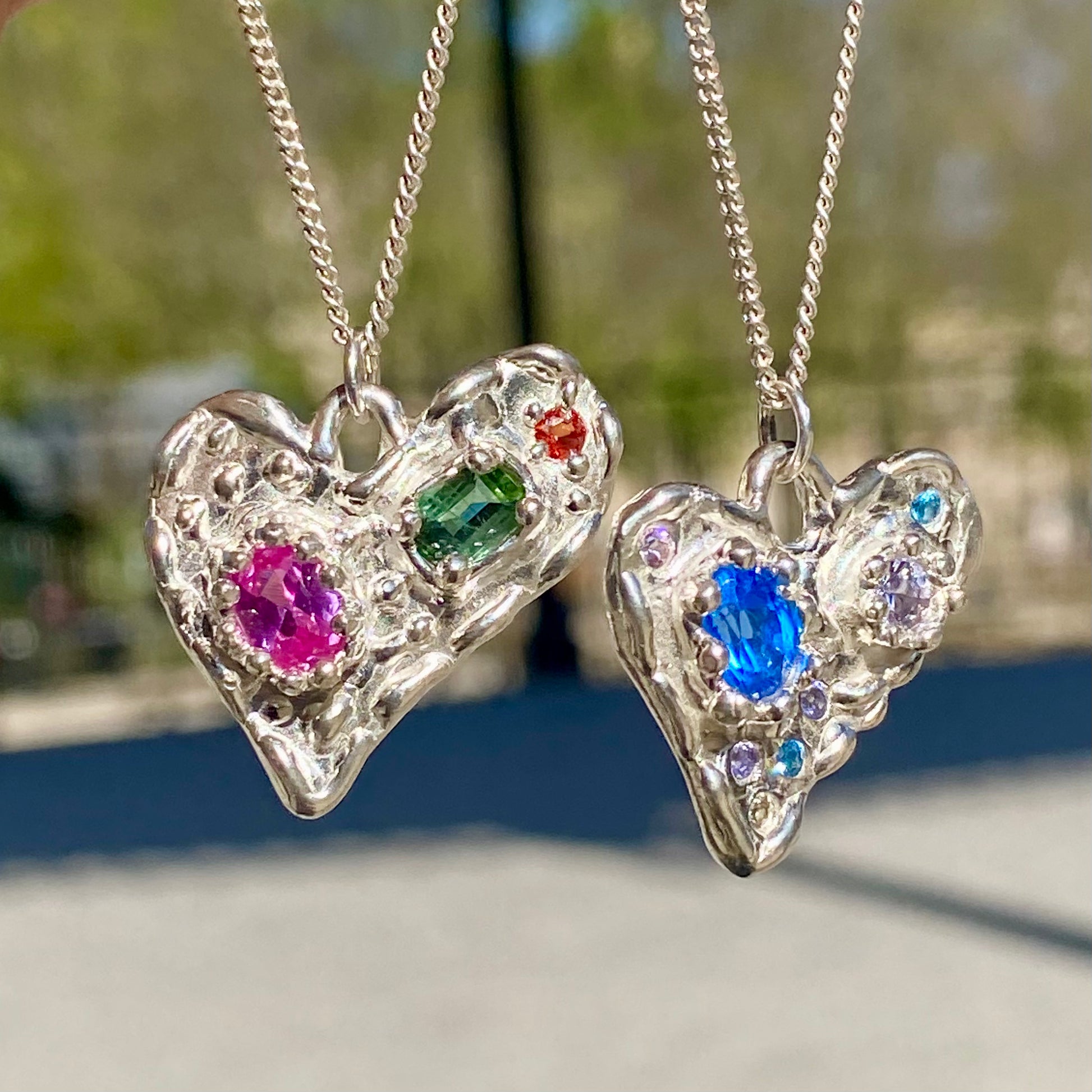 Handmade by Lia from Lia Makes Jewellery, this sterling silver heart-shaped pendant features a unique combination of colourful stones like tourmalines, sapphires, citrine, pink and blue topaz, and tiny synthetic gems, shown in a close-up to highlight the vibrant setting.
