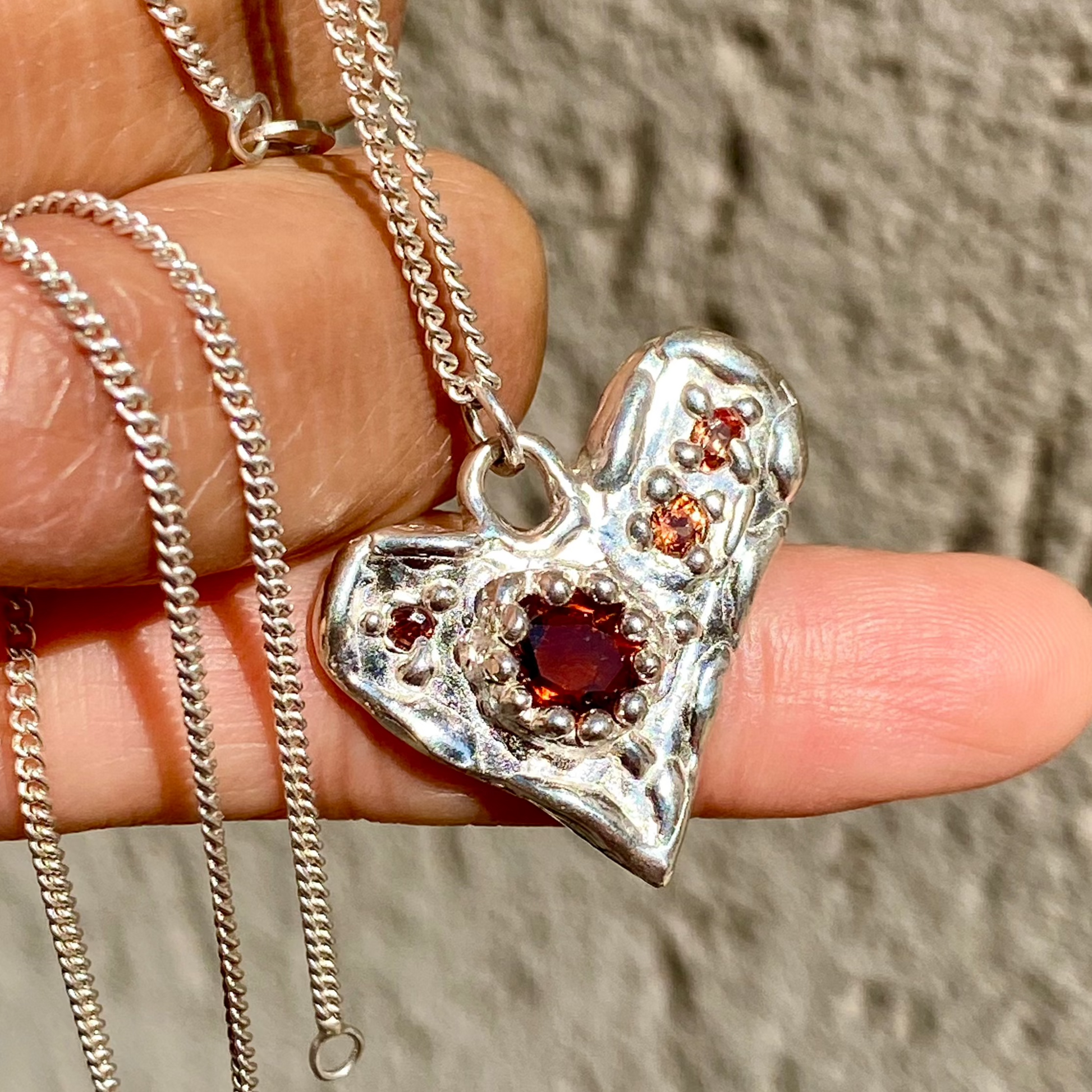 Handmade by Lia from Lia Makes Jewellery, this sterling silver heart-shaped pendant features a unique combination of colourful stones like tourmalines, sapphires, citrine, pink and blue topaz, and tiny synthetic gems, shown in a close-up to highlight the vibrant setting.
