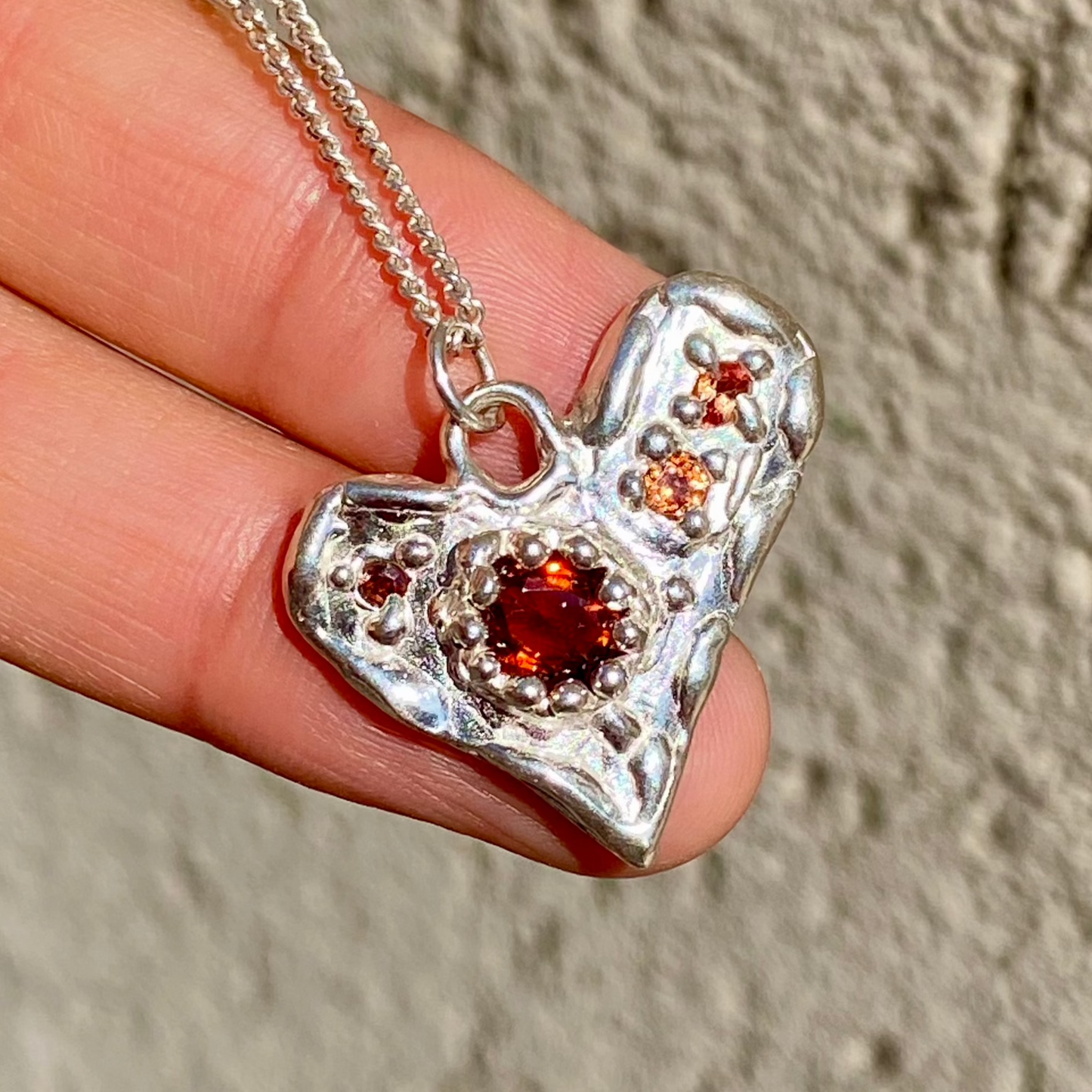 Handmade by Lia from Lia Makes Jewellery, this sterling silver heart-shaped pendant features a unique combination of colourful stones like tourmalines, sapphires, citrine, pink and blue topaz, and tiny synthetic gems, shown in a close-up to highlight the vibrant setting.
