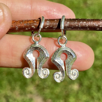 Silver Mamuli earrings held by a hand against a natural background