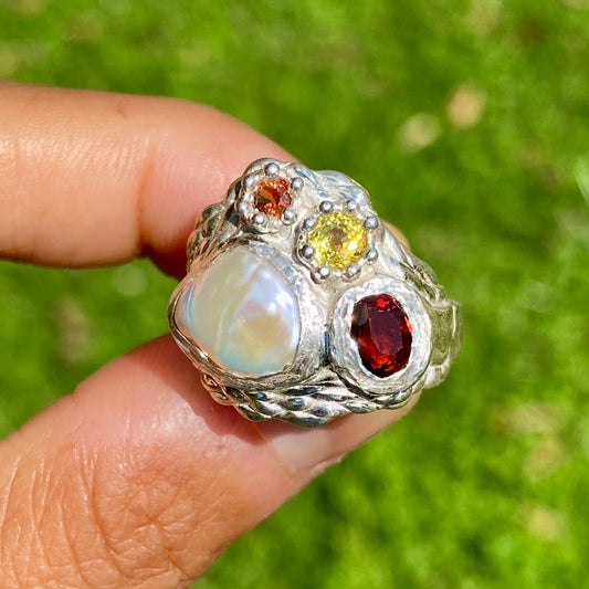 The Melodi features a thick band with four stones: a Keshi pearl, a red garnet, yellow and orange sapphires. The ring is available in size ;O 1/2 (US 7 1/4).
