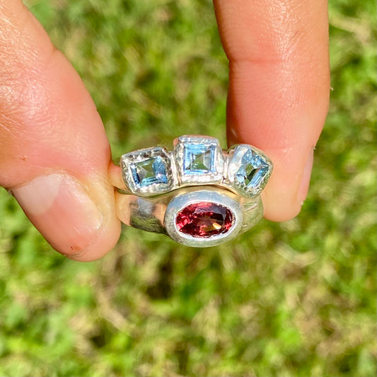 The Ocean Blossom ring stack comes as a set of two. One ring features three light blue aquamarine stones, and the other has a red oval garnet stone. Handmade by me from sterling silver, these stacking rings are available in one size: M (US 6)