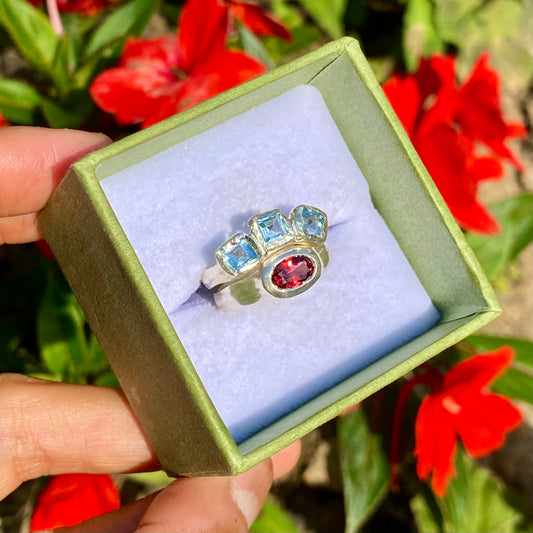 The Ocean Blossom ring stack comes as a set of two. One ring features three light blue aquamarine stones, and the other has a red oval garnet stone. Handmade by me from sterling silver, these stacking rings are available in one size: M (US 6)