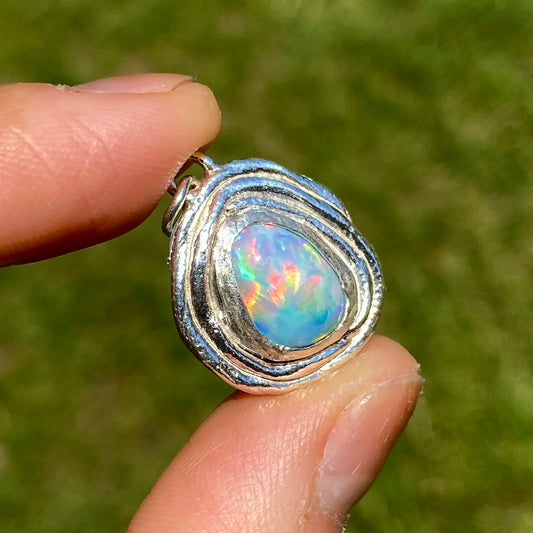 Opal pendant in a silver setting held between fingers with a blurred green background