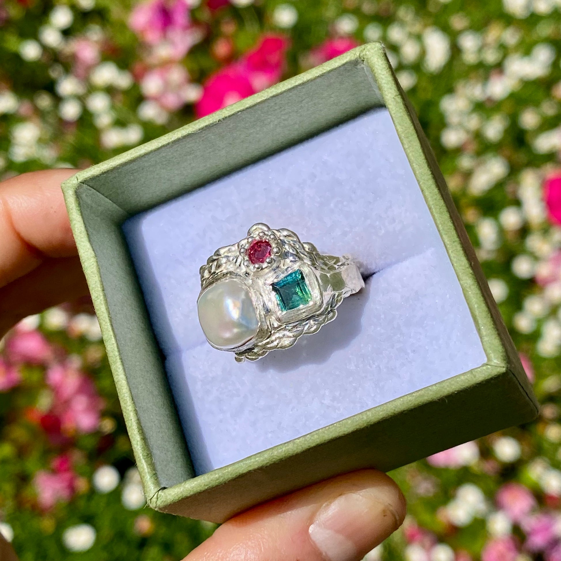 The Pearl Grove features a thick band with three stones: Keshi pearl, green square tourmaline, and pink round stone. Handmade by me from sterling silver, this ring is available in size O (US 7)