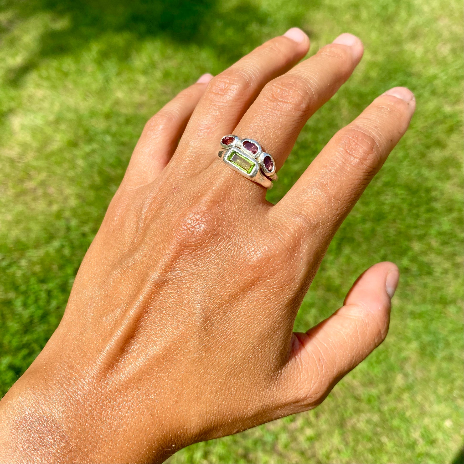 The Spring Blossom ring stack comes as a set of two. One ring features three pink tourmaline stones, and the other has a long green rectangular peridot stone. Handmade from sterling silver, these stacking rings are available in one size: O ½ (US 7 ¼).