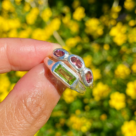 The Spring Blossom ring stack comes as a set of two. One ring features three pink tourmaline stones, and the other has a long green rectangular peridot stone. Handmade from sterling silver, these stacking rings are available in one size: O ½ (US 7 ¼).